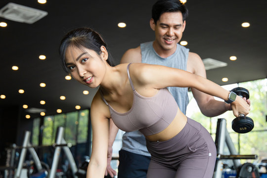 The Personal Trainer Helps Asian Women With One Arm Triceps Workout In Fitness Gym. Concepts Of Exercise For Health And Good Shape. Cinematic Tone