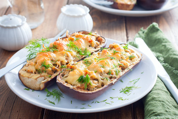Baked stuffed eggplant with minced meat with cheese on a white plate on a wooden table, selective focus