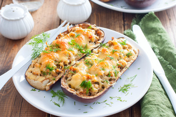 Baked stuffed eggplant with minced meat with cheese on a white plate on a wooden table, selective focus