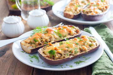 Baked stuffed eggplant with minced meat with cheese on a white plate on a wooden table, selective focus