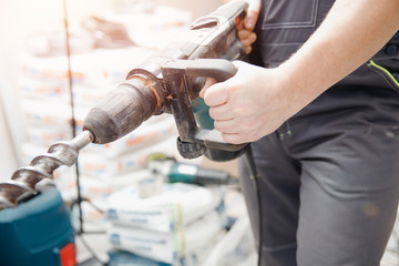 Builder worker man with hammer drill perforator equipment making hole in gray wall construction