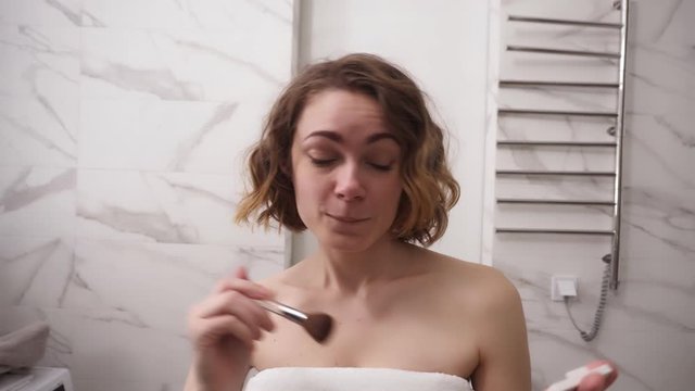 Beauty woman applying makeup. Beautiful girl applying cosmetic with a big brush. Girl gets blush on the cheekbones. Powder, rouge. Playful mood. Slow motion