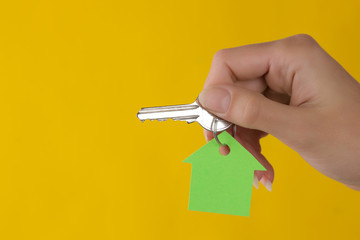 Home purchase concept. Keys with a keychain house in hand on a yellow background