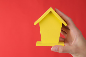 Fototapeta na wymiar Home purchase concept. Small decorative yellow house in a hand on a red background