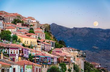 The hillside with traditional houses of Molivos, Mythimna in Lesbos island during moonrise with birds flying in the sky