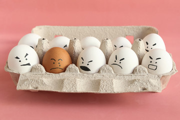 Group of white organic chicken eggs with angry faces and one brown chicken egg with crying face in...