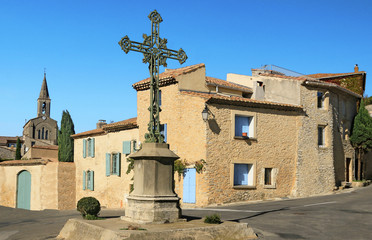 Croix monumentale sur la place d'un village provençal.
