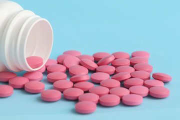 Group of pink round medicine pills and white bottle on a blue background. Selective focus. Theme of health care, medical treatment and disease prevention.