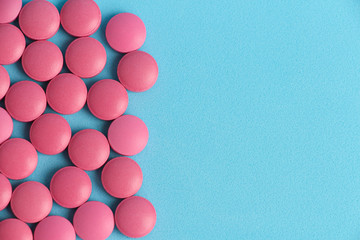 Flat lay. Group of pink round pills on a blue background. Textured background. Copy space for your text. Theme of health care, medical treatment and disease prevention.