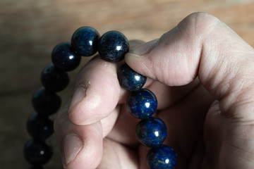Woman's right hand praying and counting dark blue beads rosary in blurred wood  background, Close up and macro shot, Select focus, Asian Body language feeling, Prayer buddhist, Religious concept