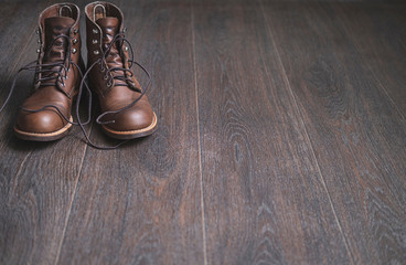 Two brown work leather men boots  with untied  laces on a wooden floor.