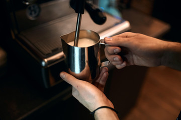 man steaming milk for hot cappuccino with machine, close up side view photo. job, profession, occupation