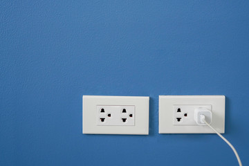 Adapter for mobile phone and electric plug on the dark blue wall.