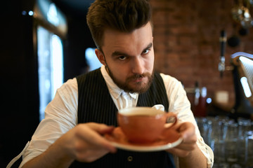 Elegant serious stict barista holding cup with lavender cappuccino, asking to taste drink .close up photo, blurred cup.