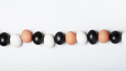 Row of eggs of different colors on a white background. Black, white and brown chicken eggs.