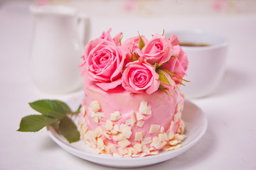 Mini small cake with pink glaze, beautiful roses, cup of coffee, gift box on the white table.