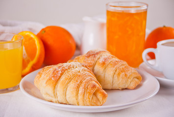 Fresh croissants buns, oranges, orange jam and juice. Breakfast concept.