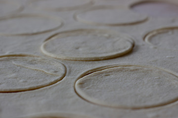 Fototapeta na wymiar Dough rolled out in a pattern for preparation of ravioli or pelmeni. The rolled out dough. Rolled into a sausage dough. Flour dough for dumplings. Cooking dumplings