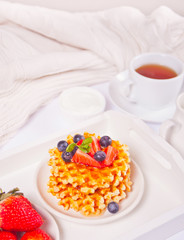 Plate with sweet tasty waffles with honey, berries, cup of tea on the white background.