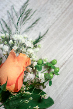 A peachy orange rose flower bud with white baby's breath (Gypsophila) and green hypericum berries against a white-washed wood background, with copy space