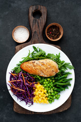 salad of chicken breast, arugula, red cabbage, carrots, corn, green peas, green beans in a white plate on a stone background