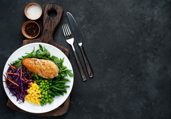 salad of chicken breast, arugula, red cabbage, carrots, corn, green peas, green beans in a white plate on a stone background with copy space for your text
