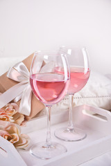 Two glasses with pink grape wine with roses and gift box on the background. Romantic dinner concept.