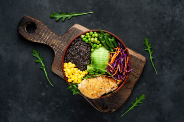 Bowl Buddha.Quinoa, chicken breast, avocado, red cabbage, arugula, carrot, green  peas, corn, broccoli, green beans in a plate on a stone background.