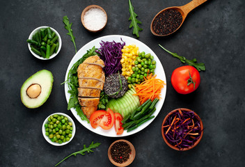 Bowl Buddha.Quinoa, chicken breast, arugula, avocado, red cabbage, carrot, green  peas, corn, tomato, green beans in a white plate on a stone background. with copy space for your text
