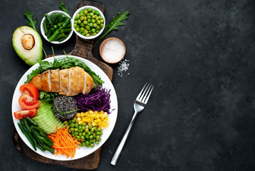 Bowl Buddha.Quinoa, chicken breast, arugula, avocado, red cabbage, carrot, green  peas, corn, tomato, green beans in a white plate on a stone background. with copy space for your text
