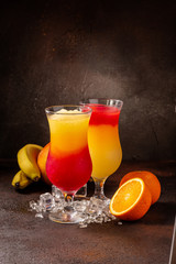 Delicious icy cocktail with fruits on dark grounge background. Healthy colorfull fruit shakes with ice on textured table.