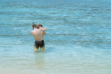 A gentleman helped wear glasses for his lover before snorkelling to see the beautiful coral in the sea.