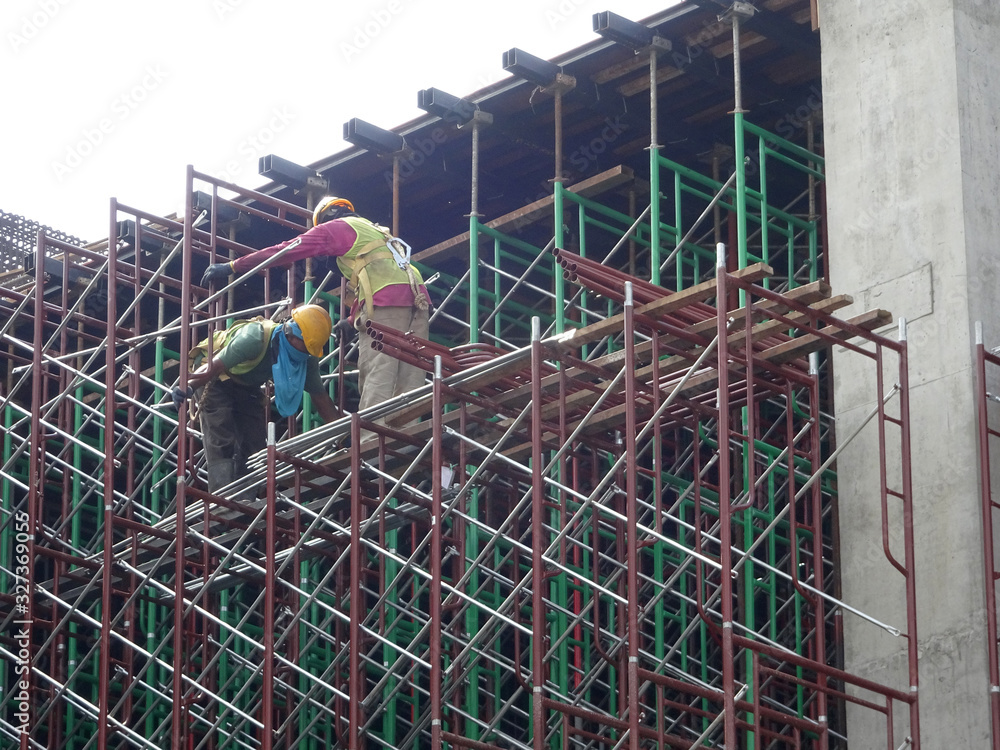 Wall mural KUALA LUMPUR, MALAYSIA -JULY 28, 2019: Construction workers wearing safety gear and safety harness while installing scaffolding at a high level in the construction site.