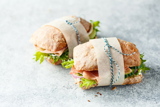 Two fresh sandwiches with ham, cucumbers, lettuce and onions on grey background.