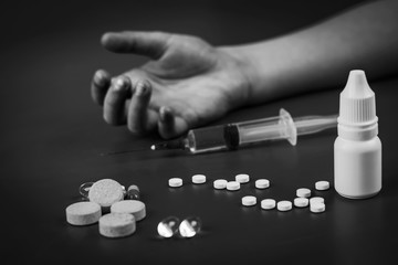 child's hand in the background no focus. In the foreground are pills. And an injection syringe. Close-up