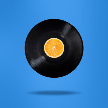 Vinyl record with orange fruit in the centre. Flying in the air. Isolated on blue background. Surrealism levitation concept.