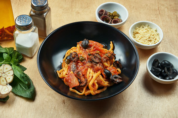 Classic, homemade pasta with olives, capers, tomatoes, anchovies in black bowl. Traditional italian cuisine. Pasta Alla Puttanesca