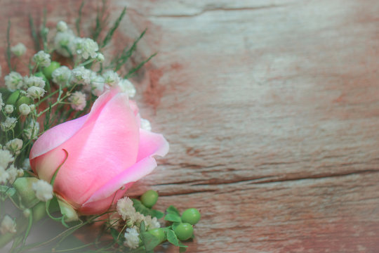A fresh pink rose flower with white baby's breath (Gypsophila) and greenery against a weathered wood background, with copy space
