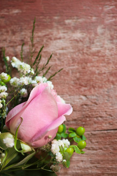 A fresh pink rose flower with white baby's breath (Gypsophila) and greenery against a weathered wood background, with copy space