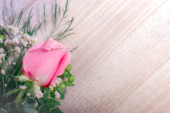 A fresh pink rose flower with white baby's breath (Gypsophila) and greenery against a white-washed wood background, with copy space