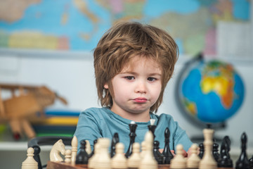 Kids early development. Concentrated little boy sitting at the table and playing chess.