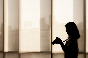 A silhouette picture of woman holding a camera to take a picture of sky scraper buildings in the modern city (black and white color)