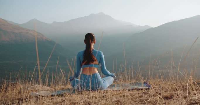 Athletic girl meditating during sunrise. Fit girl training in mountains, sitting in lotus yoga pose - healthy way of life, zennism concept 4k footage