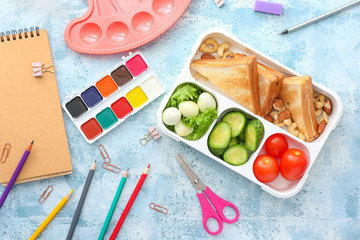 School lunch box with tasty food and stationery on table