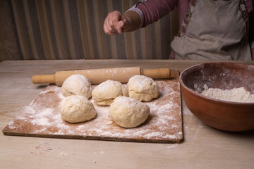 A woman kneads the dough. Plywood cutting board, wooden flour sieve and wooden rolling pin - tools for making dough.