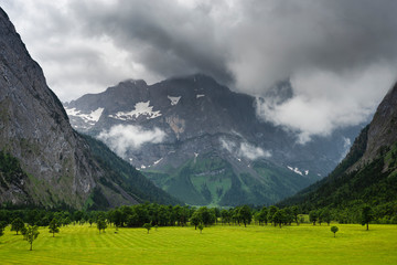 Dunkle Wolken mit Regen und kurze Aufhellungen mit Sonne über den Ahornbäumen am großen Ahornboden, Österreich,Europa