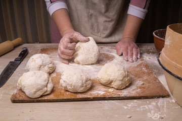 A woman kneads the dough. Plywood cutting board, wooden flour sieve and wooden rolling pin - tools for making dough.