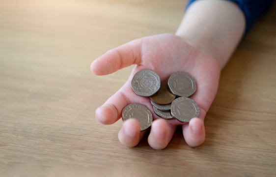 Kid hand holding coins and pennies nickels with blurry wooden table in background, Close up of children cupped hands showing British money coins, 