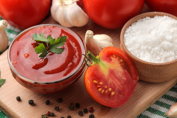 Red sauce or ketchup in a bowl and ingredients for cooking, tomatoes, garlic and spices on a natural wooden background