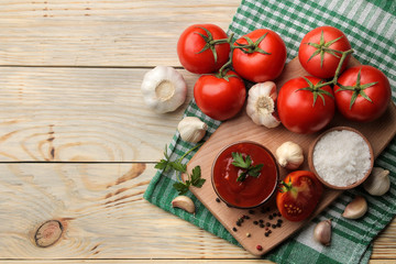 Red sauce or ketchup in a bowl and ingredients for cooking, tomatoes, garlic and spices on a natural wooden background. top view. place for text